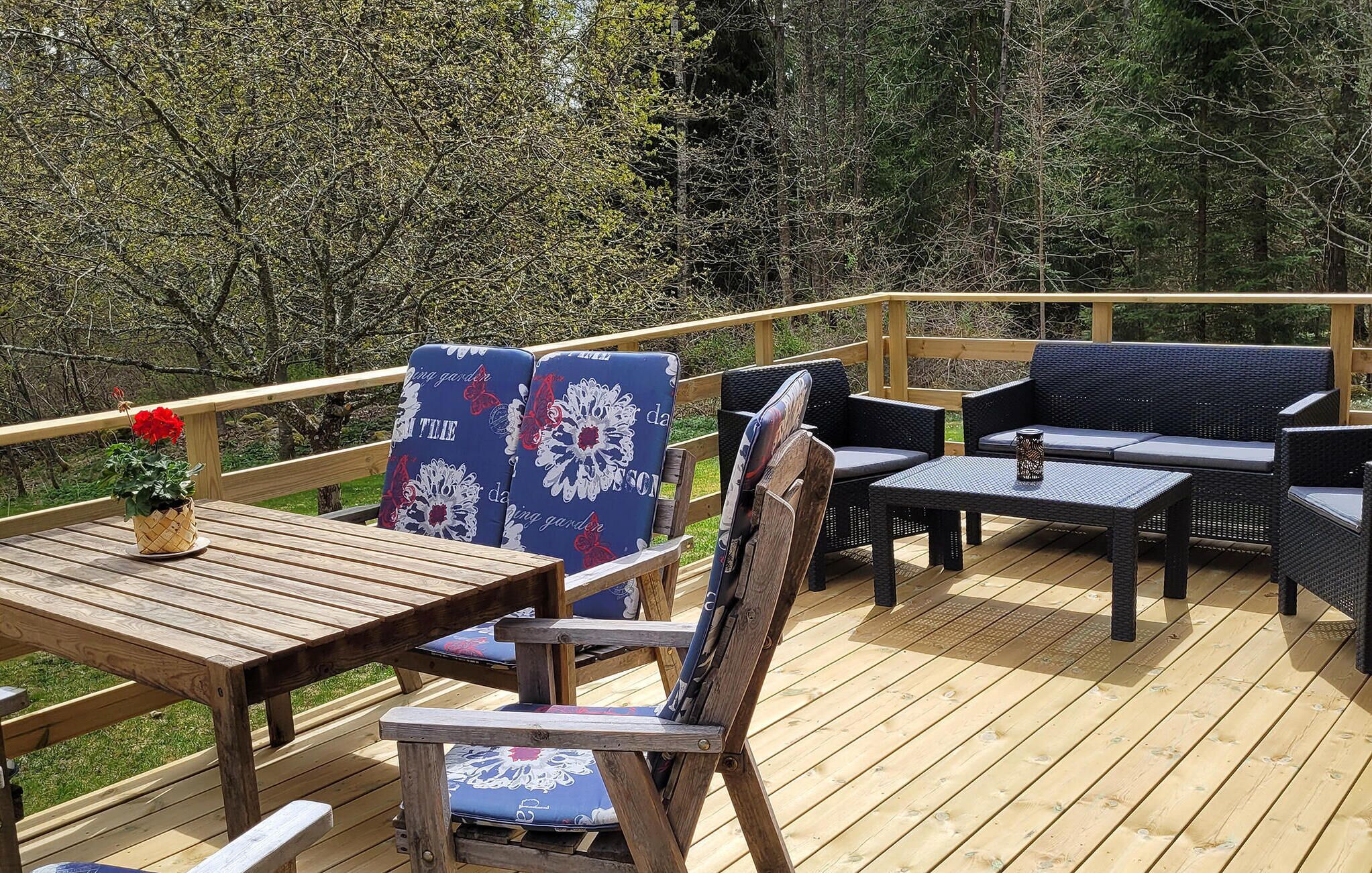 Une terrasse en bois avec des meubles d’extérieur, notamment une table et des chaises, ainsi qu’une plante en pot.