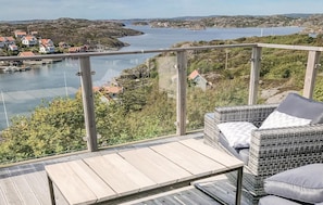 Un balcon doté de meubles en osier, donnant sur un lac où l’on aperçoit des bateaux et des maisons au loin.