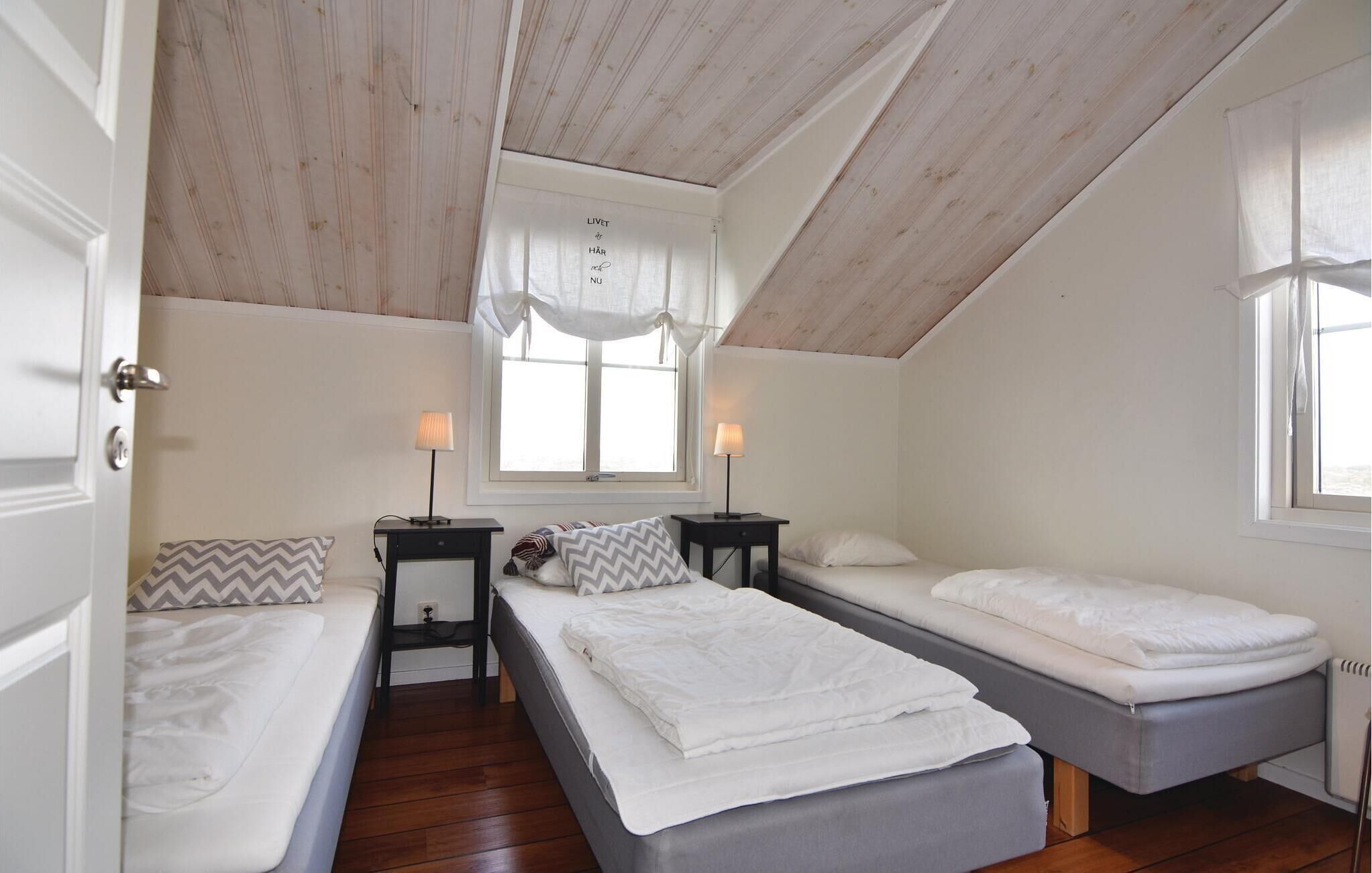 Ein Zimmer mit zwei Betten, einem fensterbelaubten Fenster, einem Deckenventilator und einem kleinen Tisch mit Lampen.