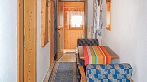Un corridoio stretto con pareti in legno e una porta in fondo. C'è una panca con una coperta a righe colorate e una sedia con motivo decorativo.