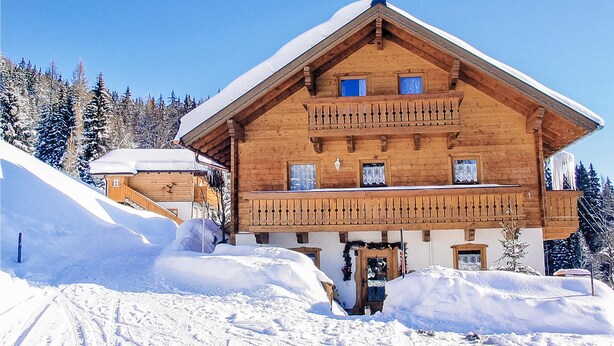 Una baita di legno con un balcone, circondata da alberi innevati.