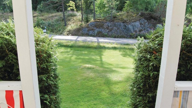 A view through a gate into a grassy area with a road in the background.