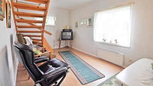 A compact living room with a wooden staircase, a black leather chair, a television, and a window with curtains.