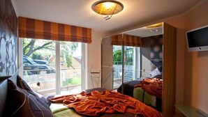 Ein Schlafzimmer mit Bett, Fenster, Fernseher und Balkon.