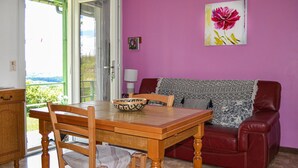 Un comedor con una mesa y sillas de madera, un sofá de cuero rojo y una pared rosa con un cuadro de flores.