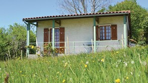Una casa rústica con techo de tejas, contraventanas de madera y una cerca verde.
