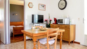 Una habitación pequeña y ordenada con una mesa de madera, un televisor, un microondas y un reloj en la pared.