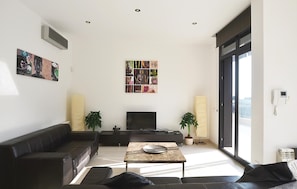 A modern living room with a sofa, a coffee table, a TV, and a large window.