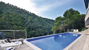 Una piscina con sillones de descanso y vistas a una ladera boscosa.