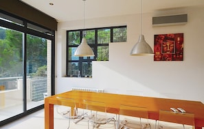 A modern dining area with a wooden table, clear chairs, pendant lights, and a view through large windows.