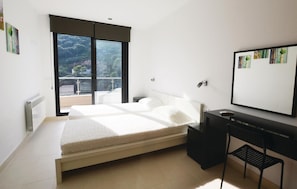 A bedroom with a bed, a desk, a chair, a radiator, and a large window with a view of trees.