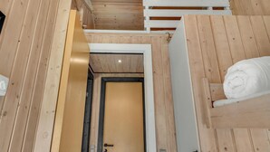 Ein Holzblockhaus-Innenraum mit einem Etagenbett, einer Tür und einem kleinen Regal mit einem zusammengerollten Handtuch.