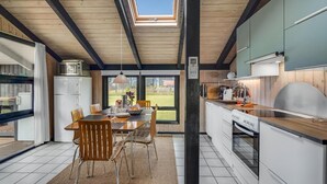 Eine moderne Küche mit Essbereich, ausgestattet mit einem großen Fenster, Holzbalken an der Decke und einem eingebauten Backofen.