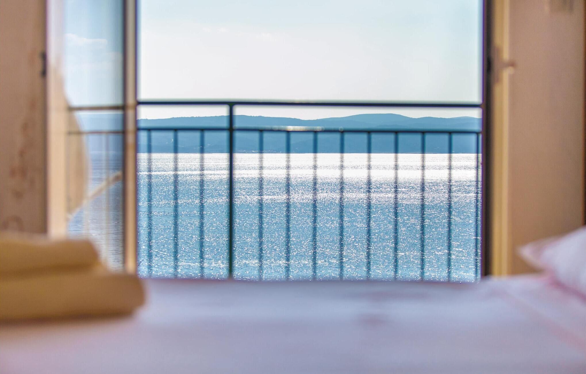 A room with a bed and a view of the sea through a window with a metal railing.