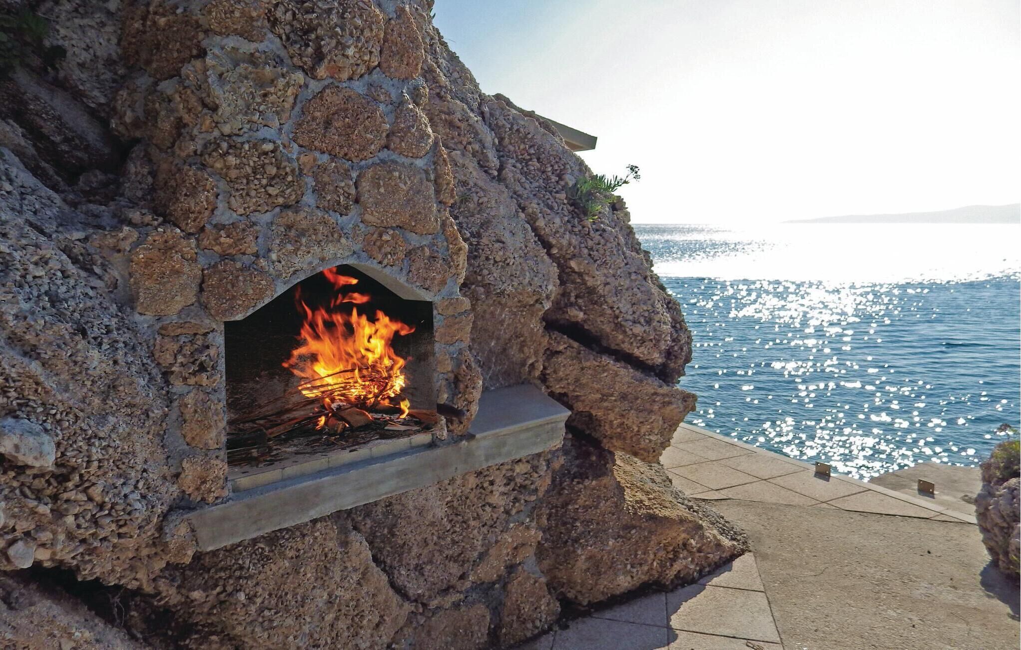 Ein Steinkamin mit Feuer, mit Blick auf ein Gewässer.