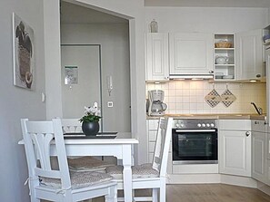 Una cocina con armarios blancos, una mesa de comedor con sillas, una cafetera y un horno.
