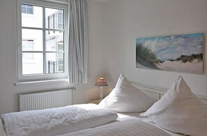 Un dormitorio con cama, ventana, radiador, lámpara y un cuadro en la pared.