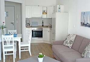 Un espacio habitable compacto con kitchenette, una mesa de comedor con sillas, un sofá y una planta en maceta.