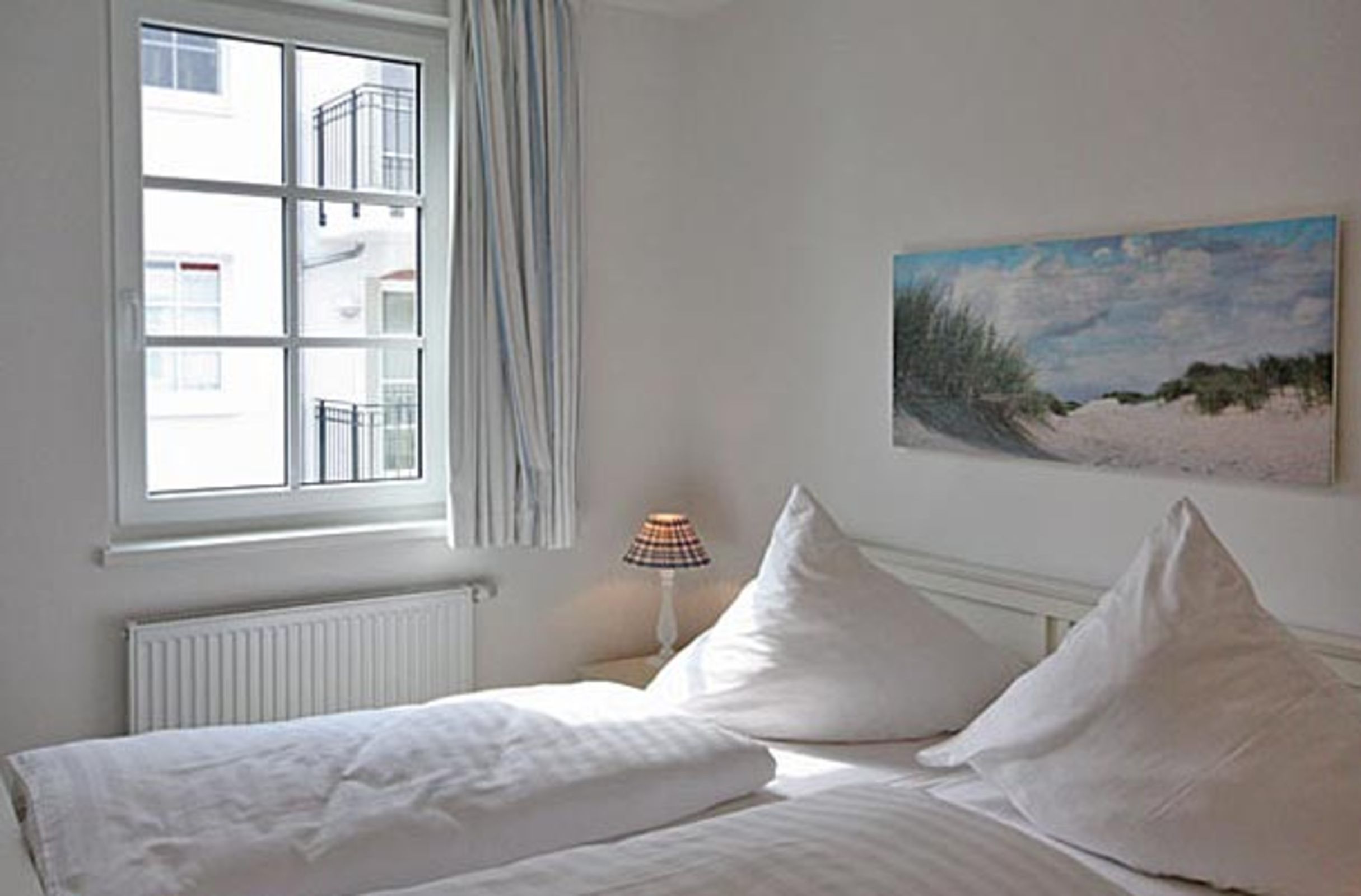 Et soveværelse med seng, et vindue, en radiator, en lampe og et billede på væggen.