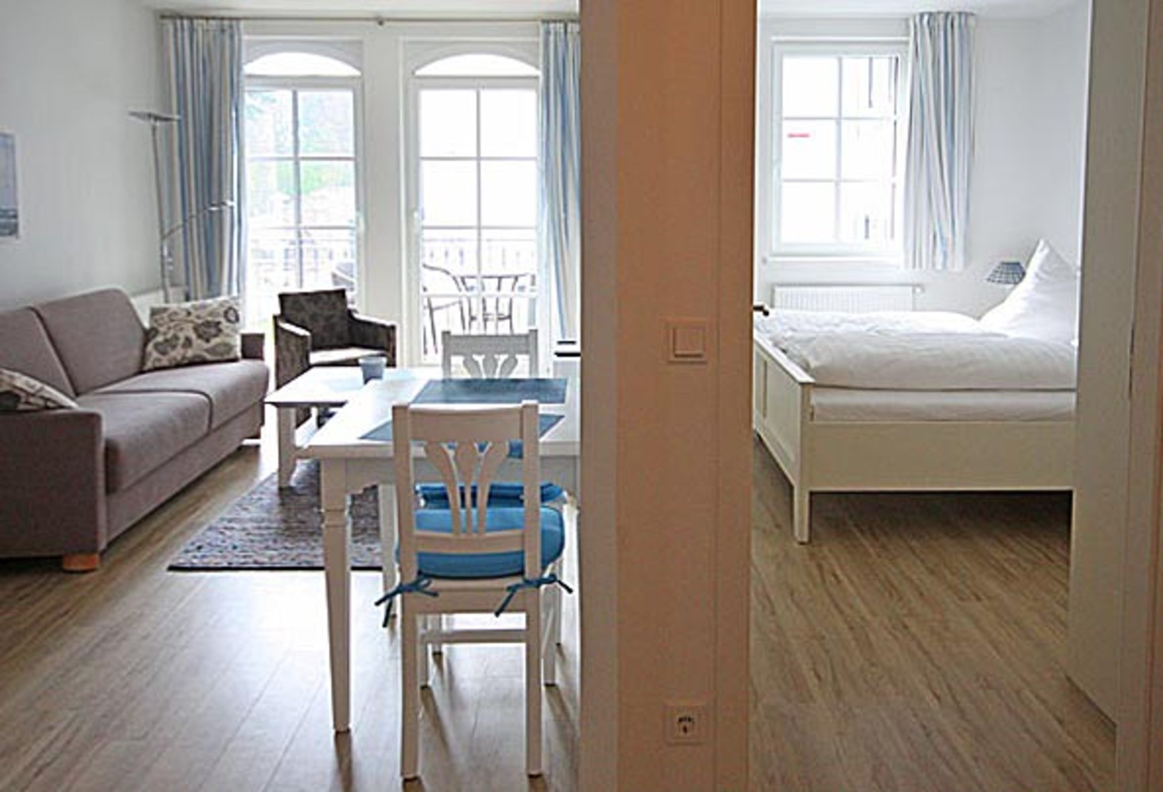 A room with a sofa, a dining table with chairs, a bed, and large windows with curtains.