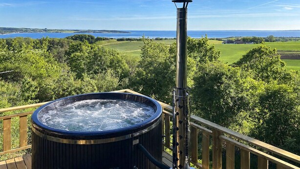 Un bain à remous sur une terrasse offrant une vue sur un lac et la verdure environnante.