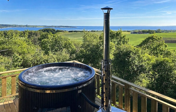 A hot tub on a deck with a view of a lake and greenery.