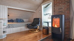 Une pièce chaleureuse avec un lit en mezzanine, un fauteuil en cuir noir, un poêle à bois et un plancher en bois.