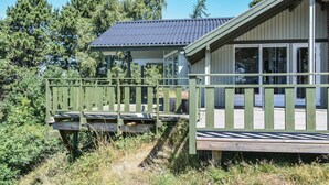 Une terrasse en bois avec une rambarde, un espace couvert doté d’un toit en métal et un bâtiment avec de grandes fenêtres.