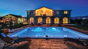 Ein zweistöckiges Haus mit Schwimmbad, Sitzgelegenheiten im Freien und einer überdachten Terrasse.