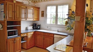A kitchen with wooden cabinets, a microwave, a coffee maker, and a window with a view of greenery. - 6 bedroom stunning home in Pénestin (Pénestin)