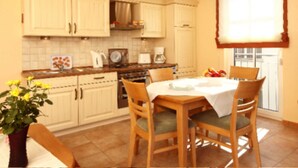 Una cocina con armarios blancos, estufa, cafetera y una mesa de comedor con sillas.