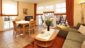 Una sala de estar con sofá, una mesa de comedor con sillas, televisión y ventana con cortinas.
