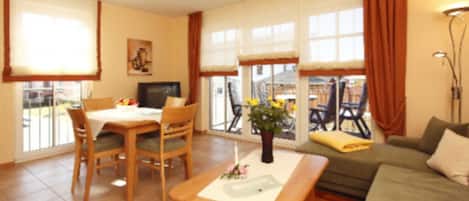 A living room with a sofa, a dining table with chairs, a TV, and a window with curtains.