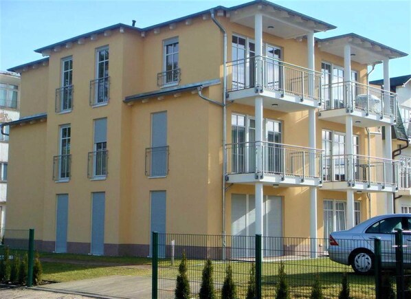 A multi-story residential building with balconies, a car parked in front, and a fenced yard. - Butcher, Villa Ilona - Apartment Villa Ilona (Heringsdorf)