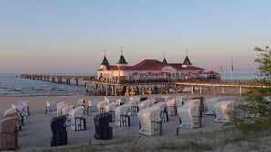 A beachside building with a pier extending into the sea, featuring a restaurant with outdoor seating and a view of the ocean. - Butcher, Villa Ilona - Apartment Villa Ilona (Heringsdorf)