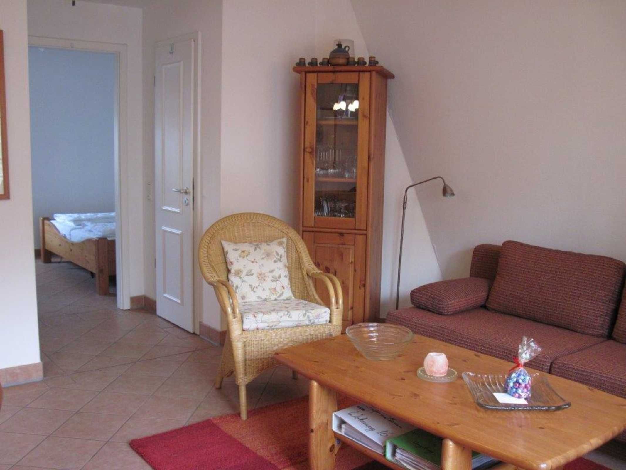 A cozy living room with a wicker chair, a wooden table with a bowl and a book, a red sofa, and a tall wooden cabinet with glass doors.