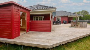 A red wooden structure with a door, a covered patio area with outdoor furniture, and a satellite dish. - Beautiful home in Broager with sauna (Broager)