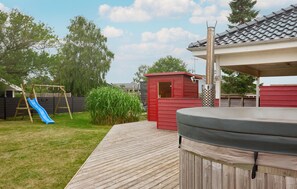 A backyard with a wooden deck, a hot tub, a red playhouse, and a blue slide. - Beautiful home in Broager with sauna (Broager)