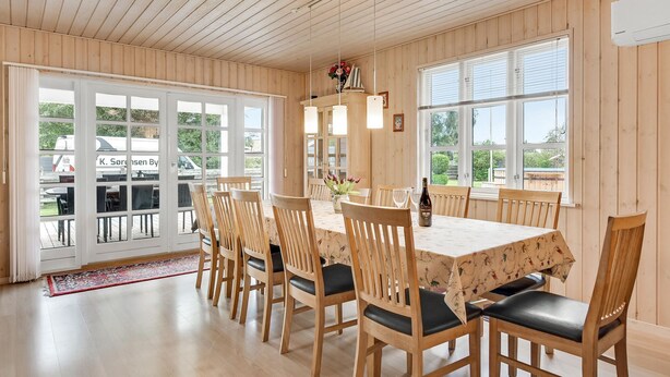 A dining area with a wooden table and chairs, large windows, and a view of the outside. - Beautiful home in Broager with sauna (Broager)