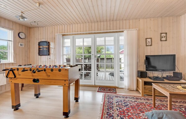 A cozy room with a foosball table, a television, and a large window with a view of the outdoors. - Beautiful home in Broager with sauna (Broager)