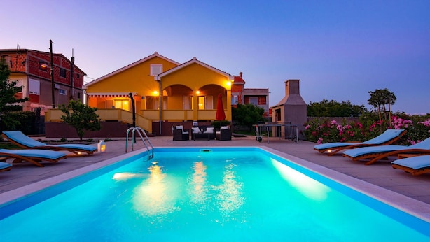 A swimming pool with lounge chairs and a building with a yellow facade in the background. - Beautiful home in Vrsi (Vrsi)