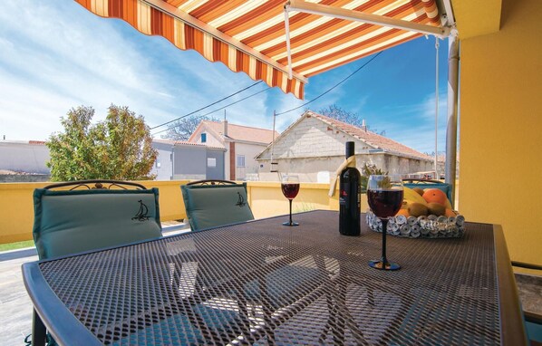Une terrasse extérieure avec une table, des chaises, une bouteille de vin et un panier de fruits.