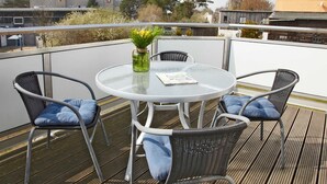 Et rundt glasbord med fire stole, en vase med gule blomster og et magasin på bordet.