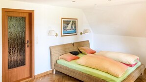 Ein Schlafzimmer mit einem Korbmöbelbett, einer Holztür mit Glasfenster, zwei Wandlampen und einem gerahmten Bild eines Segelboots.
