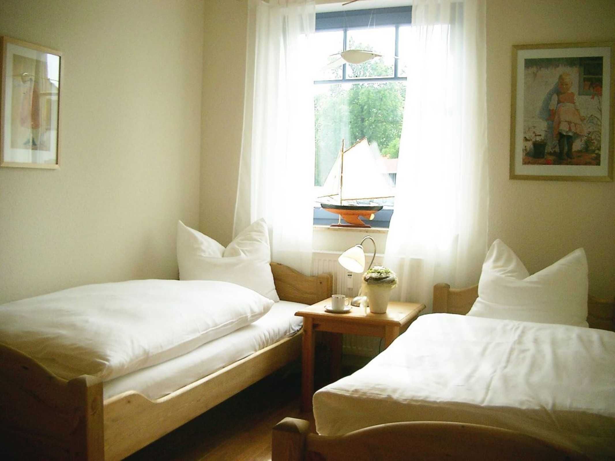 A room with two single beds, a small table with a lamp, and a window with a view of greenery outside.