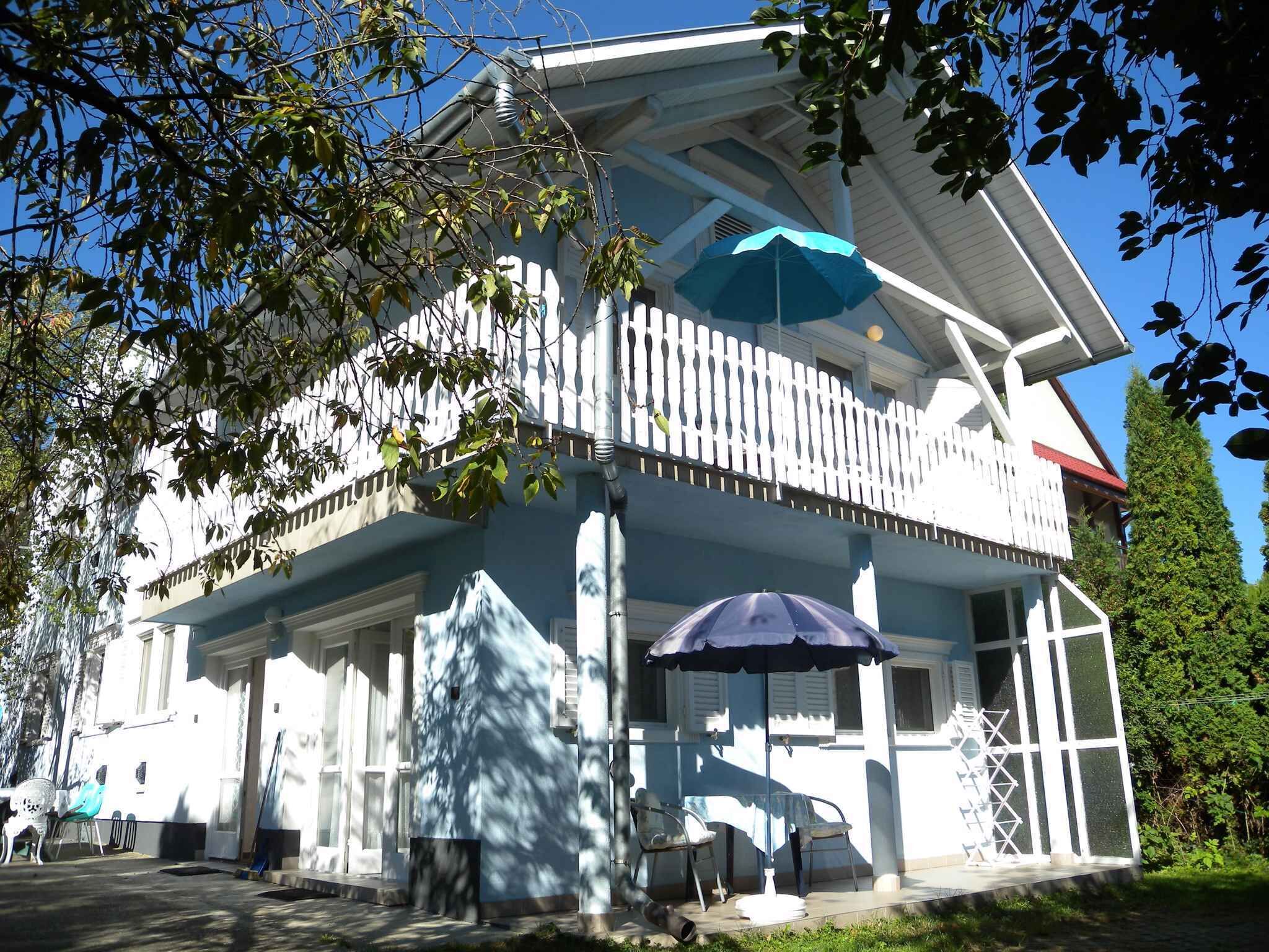 A two-story building with a balcony, a covered outdoor seating area, and a white fence.