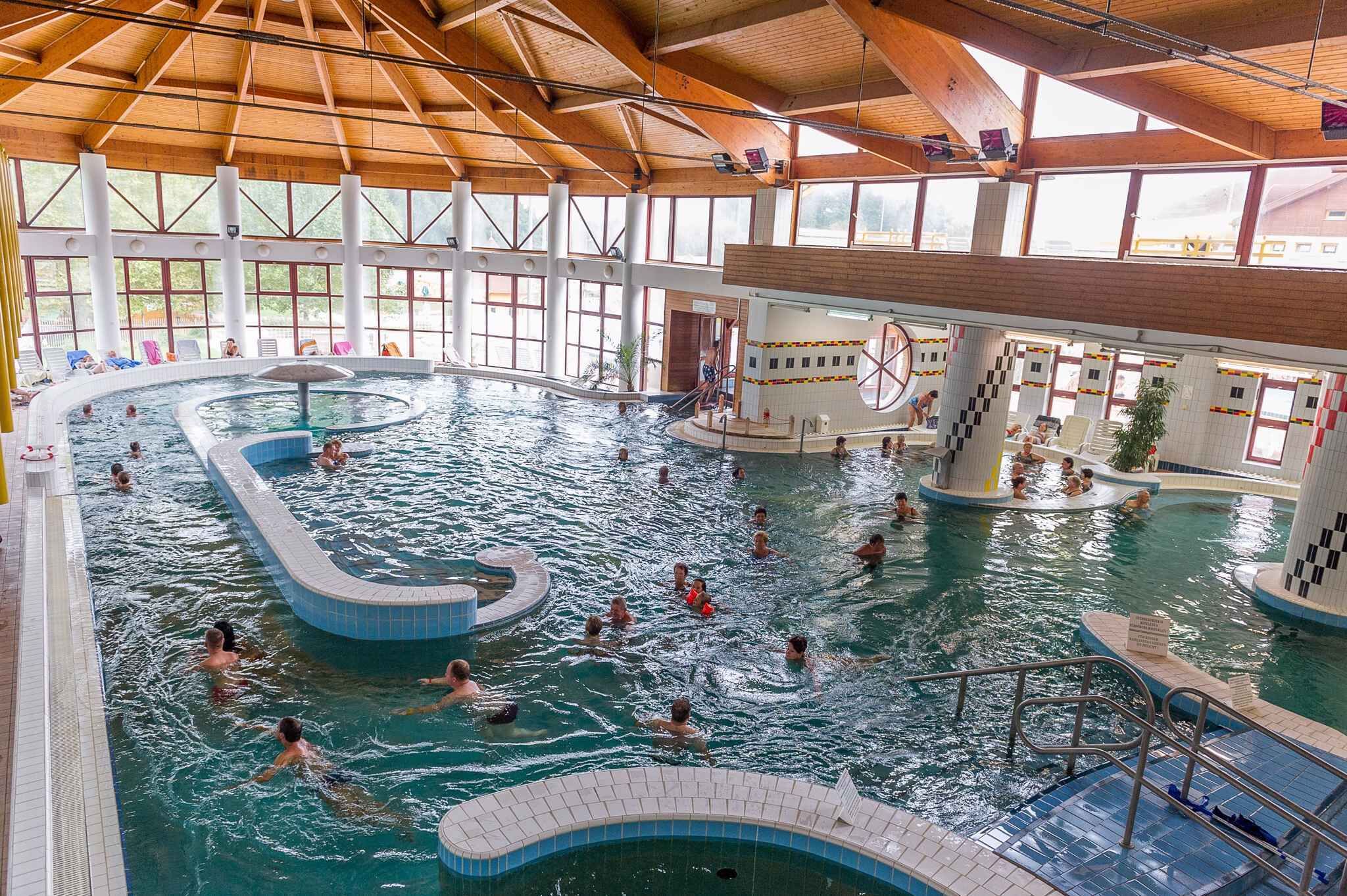 En indendørs swimmingpool med flere baner, en central fontæne og et tilskuerområde med stole.