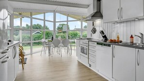 Una cocina moderna con armarios blancos, un ventanal grande y una zona de comedor con mesa y sillas.