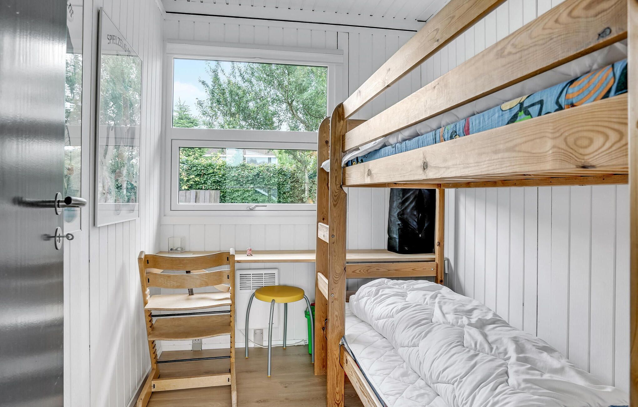 A compact room with a bunk bed, a desk with a chair, and a window overlooking greenery.