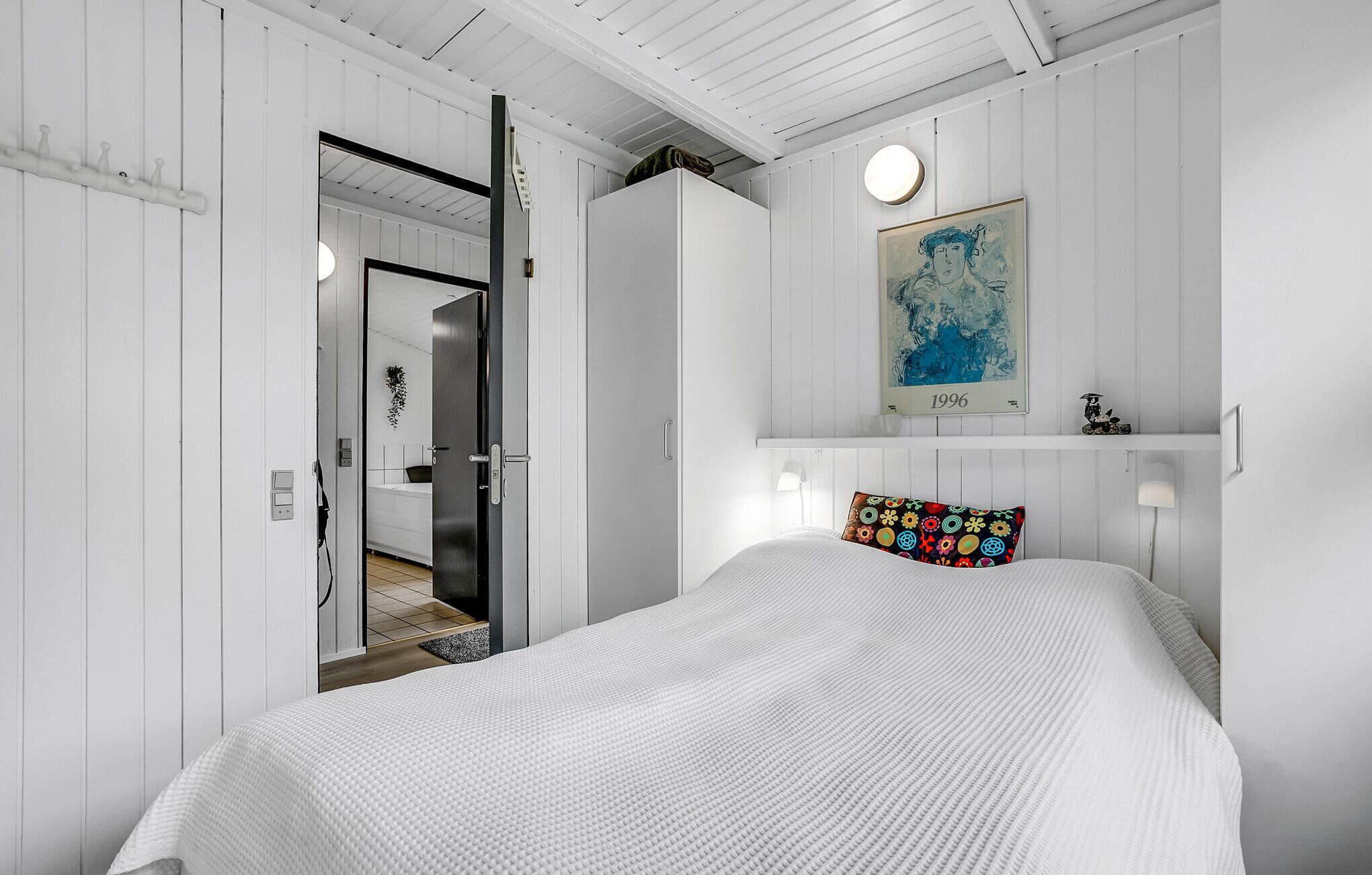 Una camera da letto con un letto, una porta che dà su un bagno, uno scaffale a parete con un quadro e un cuscino colorato.